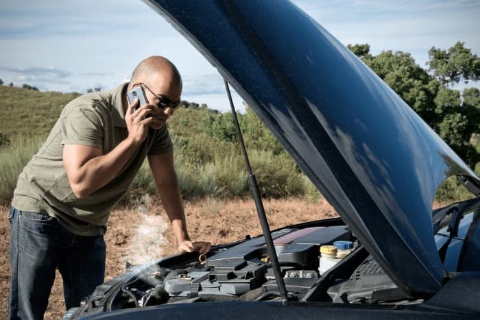 person with a broken car and the hood up looking at steam coming from an engine