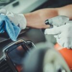Someone holding a DIY cleaner for car interior and cleaning the dashboard
