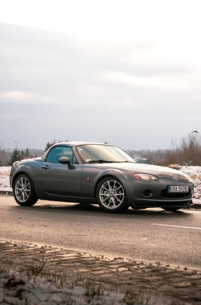 grey miata parked on the road with some snow on the side